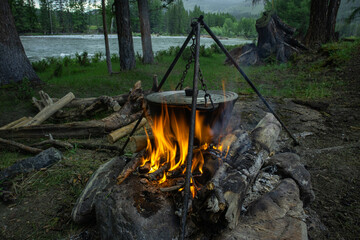 Tourists prepare lunch in a camping pot on a campfire. Cooking in the forest on the banks of a mountain river outdoors. Travel camp, campfire site.