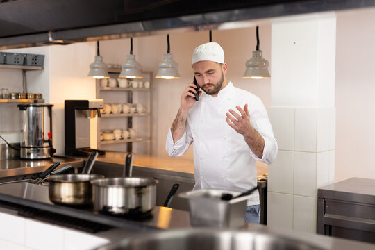 Focused caucasian male chef talking on smartphone, gesticulating in restaurant kitchen, copy space