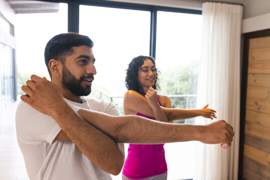 Happy biracial couple stretching practicing yoga and smiling in sunny room at home