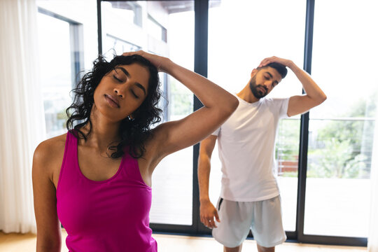 Happy biracial couple stretching, practicing yoga and smiling in sunny room at home