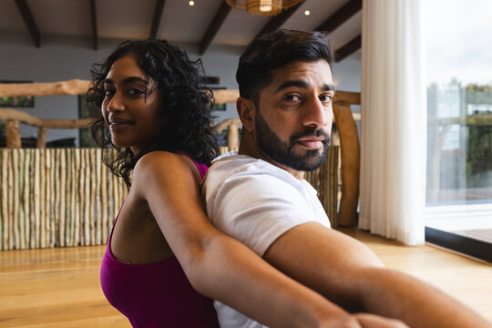 Happy biracial couple exercising practicing yoga in sunny room at home