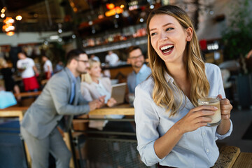 Portrait of happy young business woman drinking coffee in a break. In the background, her colleagues