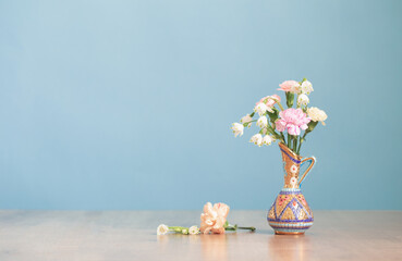 flowers in vintage jug on wooden table on blue background