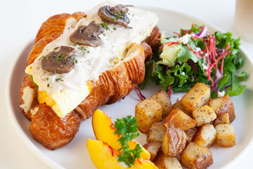 Mushroom cream cheese and scrambled egg brioche croissant sandwich with peach, rocket leaves feta cheese and sautéed potatoes.