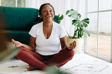 Happy senior woman meditating in lotus position at home