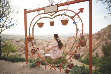 Girl sitting on a decorated heart-shaped bench on a viewpoint and admiring view of Cappadocia
