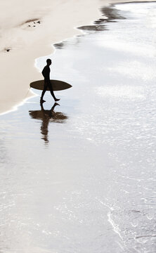 Silhouette of surfer going to riding in water of Bay of Biscay in shiny wet sand