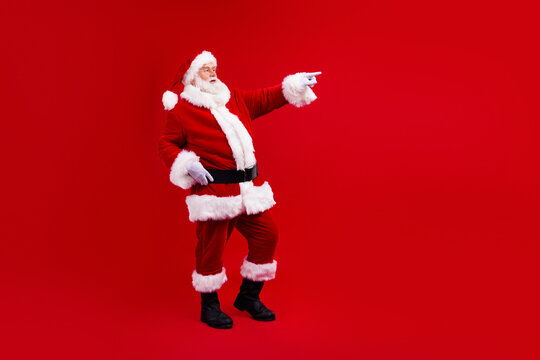 Side profile photo of positive grandfather wear stylish santa costume look directing at sale empty space isolated on red color background