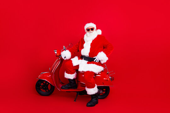 Photo of cool good mood grandfather wear stylish santa costume in glasses sit on moped hand on waist isolated on red color background