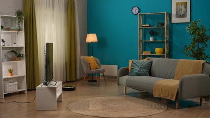 Home living room with sofa and TV screen, closets and chair, robot vacuum cleaner on the floor....