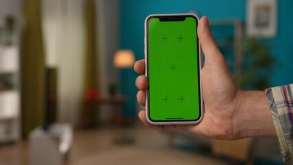 Man hand holding smartphone with Chroma key green screen. Advertising area workspace mockup. Smart home concept.