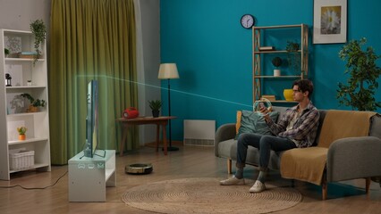 Young man sitting on the sofa in the living room holding smartphone turning on TV, infographic overlay. Smart home concept.