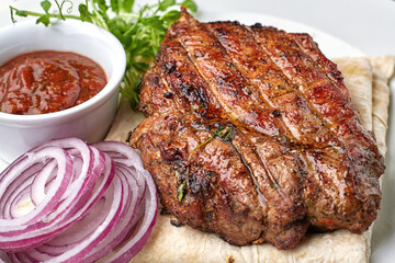 Grilled meat steak with onions, sauce and microgreen, on pita bread, on a white plate, against a dark background. space for text.