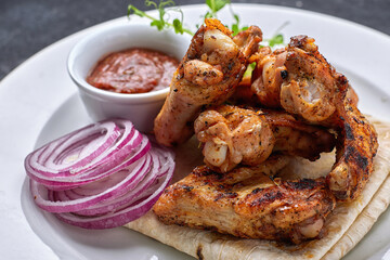Grilled chicken wings with barbecue sauce, pita bread, microgreen and onion rings, on a white plate