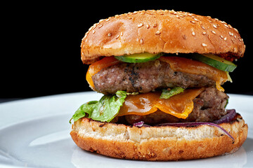 Burger with double meat cutlet, cheese. cucumber, and lettuce, on a white plate, on a black background