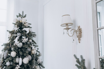 Cozy flat apartment photo studio room green Christmas Tree gifts presents garlands, candles white decorated toys balls interior New Year lights glowing bokeh
