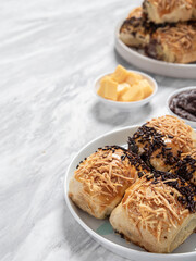Bolen Pisang or Banana Wrapped is neatly presented on a white plate with decorations around it, isolated against a white and gray table background.