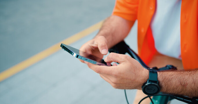Close up man hands holdilg mobile phone. Unrecognizable male cyclist use smartphone typing a message and while standing near bike.