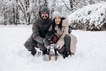 Fototapeta na wymiar Young couple having fun with dog in winter family portrait, snowy season in city park, holiday vacation weekend, enjoying spending time together