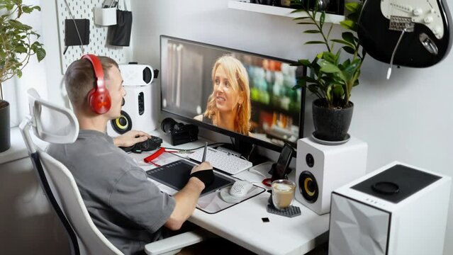 A male photographer in a comfortable home office processes and edits a photo on a personal computer using a stylus and tablet.