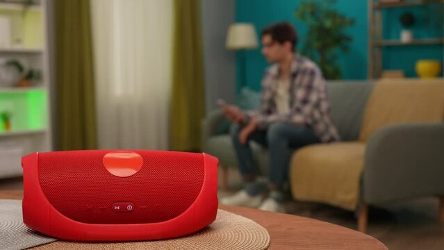 Man sitting on the sofa holding smartphone and turning on speaker using phone app. Smart house concept.