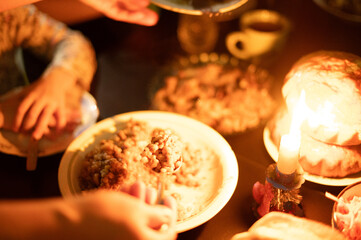 Christmas Eve in a Ukrainian family. Kutya on the table and a lighted candle. The child collects kutya porridge with a spoon.