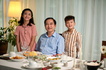 Portrait of senior Vietnamese man and his two grandkkids sitting at dinner table
