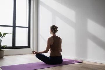 Poster Young woman practicing yoga near floor window in yoga studio, Young girl meditating at home, Harmony, balance, meditation, relaxation, healthy lifestyle concept  © kite_rin