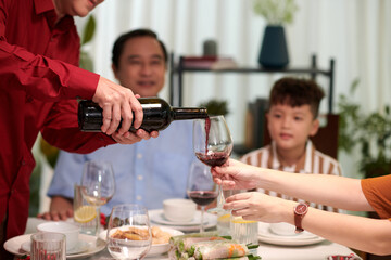 Hands of man pouring wine in glass of family member at dinner