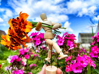 Wooden toy man with flowers in hand of woman and background grass. Concept of holiday, gift...
