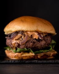 Juicy Homemade burger with lettuce onions, and chipotle sauce in a brioche bun. Dark and moody background.