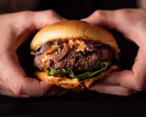 Juicy Homemade burger with lettuce onions, and chipotle sauce in a brioche bun. Dark and moody...