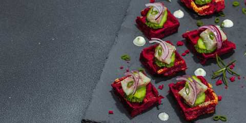 A delicious festive appetizer with herring on pieces of beet waffles with spices and sauce