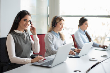 Portrait of female call center worker accompanied by her team. Smiling customer support operator at work.