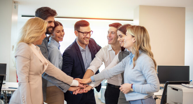 Happy business co-workers stacking hands at office. Community team spirit and cohesion. Supporting hands.