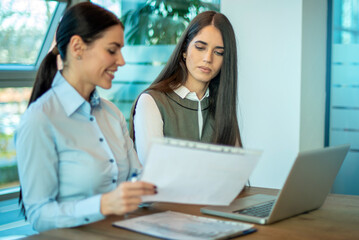 Business women discussing paperwork at the meeting while using laptop in office.