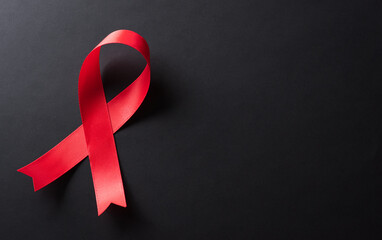 Closeup red ribbon HIV, world AIDS day awareness ribbon on black background. Healthcare and medicine concept. - obrazy, fototapety, plakaty