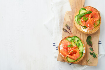 Open smoked salmon sandwiches with cream cheese, cucumber, sesame seeds, microgreens, spinach, and peas leaves on light old wooden background. Healthy breakfast food. Delicious snack. Top view.