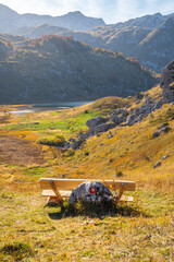 A wooden bench next to the hiking trail with a view of the lake, hills, peaks and rocks with beautiful colors in autumn