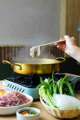 shabu-shabu, sukiyaki, hand using chopsticks to pick up a thin slice of pork put it into the pot. 