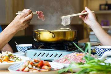 shabu-shabu, sukiyaki, hand using chopsticks to pick up a thin slice of pork put it into the pot. 