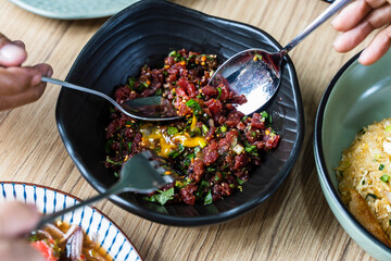 eating Spicy raw beef salad with minced meat and raw eggs on top