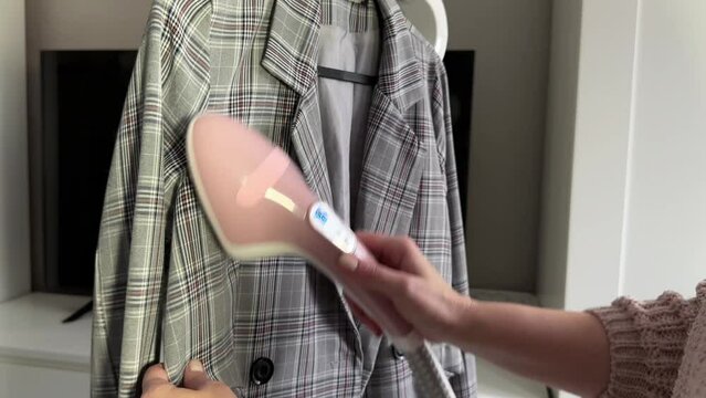 woman steams office clothes plaid jacket with electric steamer at home, dry cleaning clothes