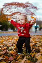 My little daughter plays with autumn leaves in the city park. Cute baby girl playing outdoors.