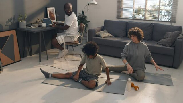 Full shot of multiethnic family of three doing different activities together while staying in same room