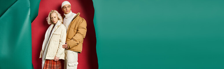 stylish man and woman in winter jackets posing together on torn turquoise and red background, banner