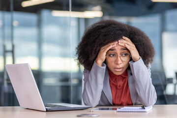 Frustrated and tired depressed business woman sitting at workplace inside office, unhappy african...