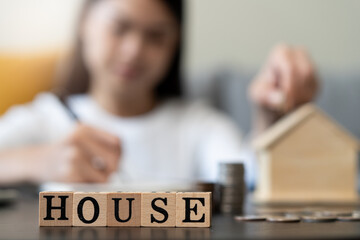 Close up hands of Woman putting coin into piggy bank house model  saving for buy property