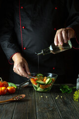 The chef is preparing a vegetable salad for lunch in the kitchen. Adding vegetable oil to vitamin salad. Space for a recipe on a dark background