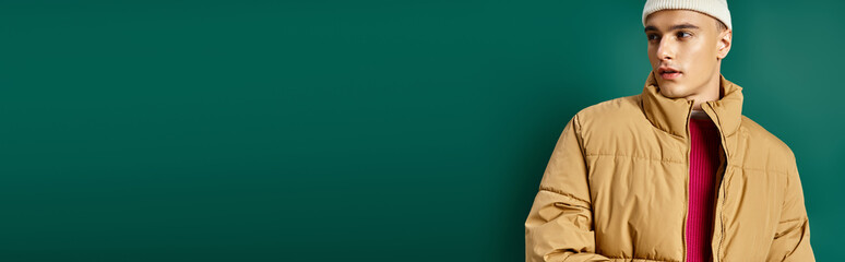 banner of handsome man in beanie hat and stylish puffer jacket on turquoise background, winter trend © LIGHTFIELD STUDIOS
